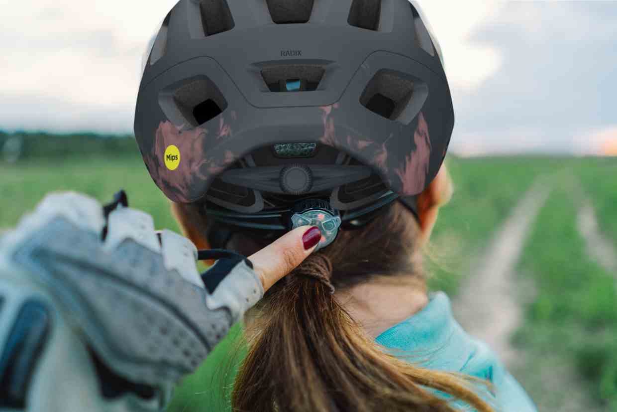 Ciclista de costas ajustando seu capacete Giro Radix MIPS cinza na cabeça.