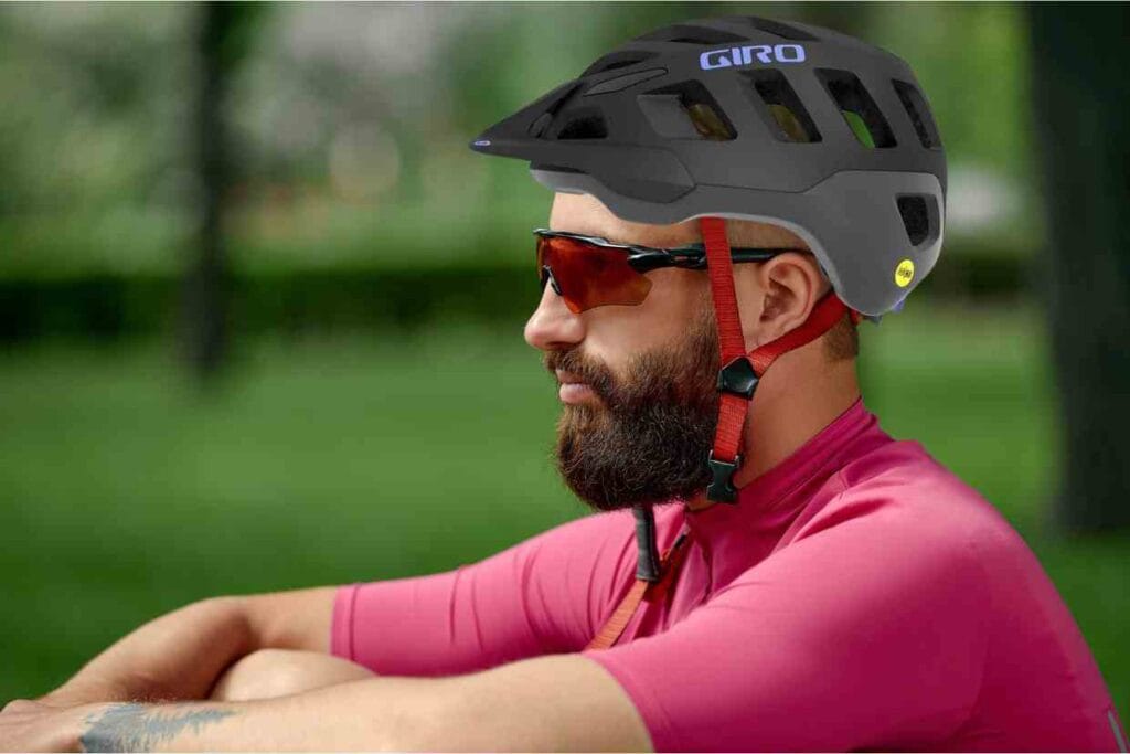 Ciclista sentado no chão com olhar fixo a frente, vestindo uma camisa rosa e o capacete Giro Radix MIPS cinza na cabeça.