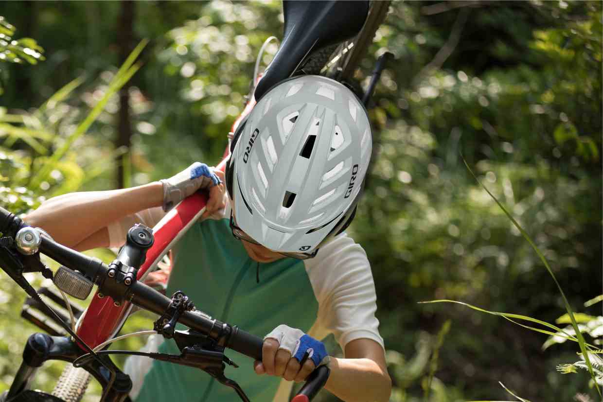 Uma ciclista usando seu capacete Giro Radix MIPS carrega sua bike no ombro por uma trilha fechada.