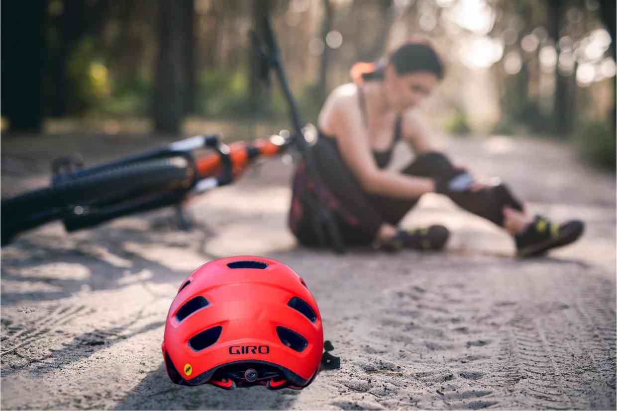 Ciclista caída ao lado da sua bike, tendo seu capacete mtb Giro Chronicle MIPS vermelho sobre o chão.