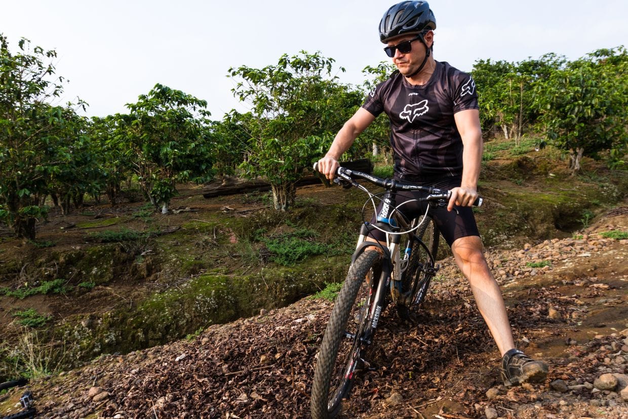 Ciclista na sua bike MTB apoiando um dos pés no chão enquanto manobra numa trilha inclinada, usando sua bermuda Barbedo Sprint preta.